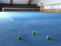 Innenansicht der Tennishalle des Tennisclub Dettenhausen mit hellblauem Teppichboden und Granulat
